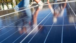Técnico com luvas instala painéis solares fotovoltaicos, vistos de perto e refletindo o céu