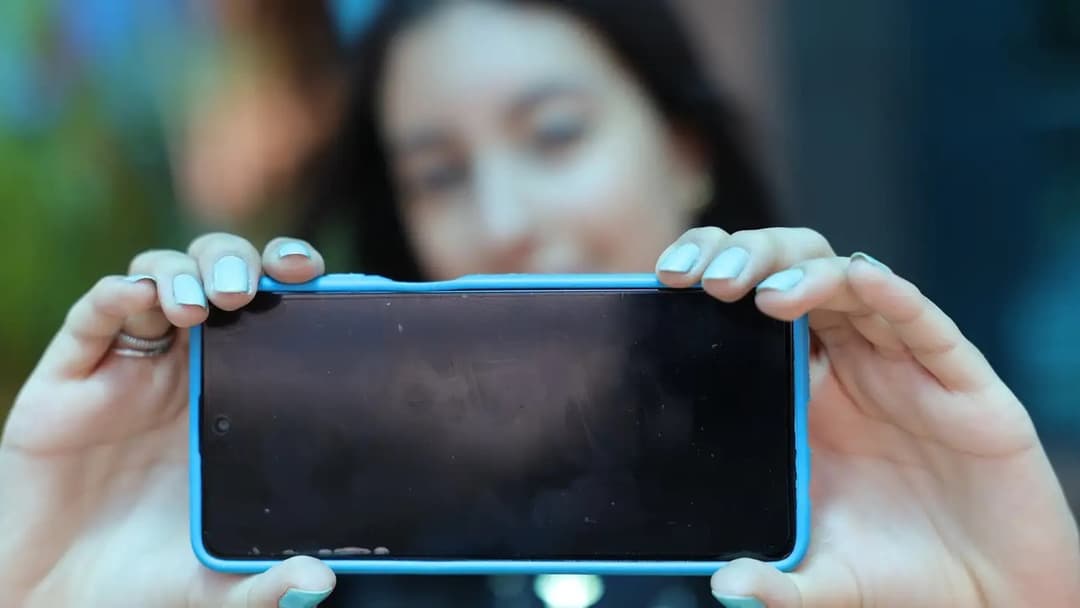 Jovem segura um celular em direção à câmera, mostrando a tela do aparelho, foto ilustrativa de uso de redes sociais