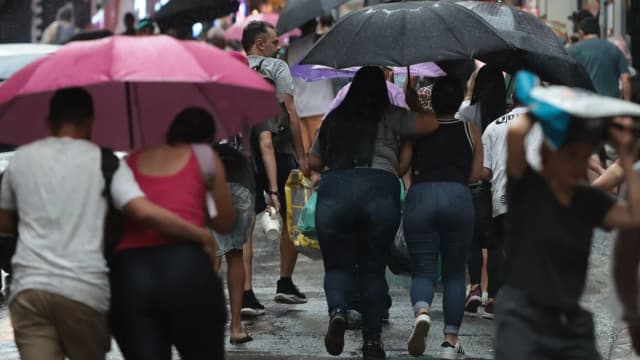 Pessoas caminham sob chuva forte protegidas por guarda-chuvas em via urbana (foto de arquivo, ilustrativa)