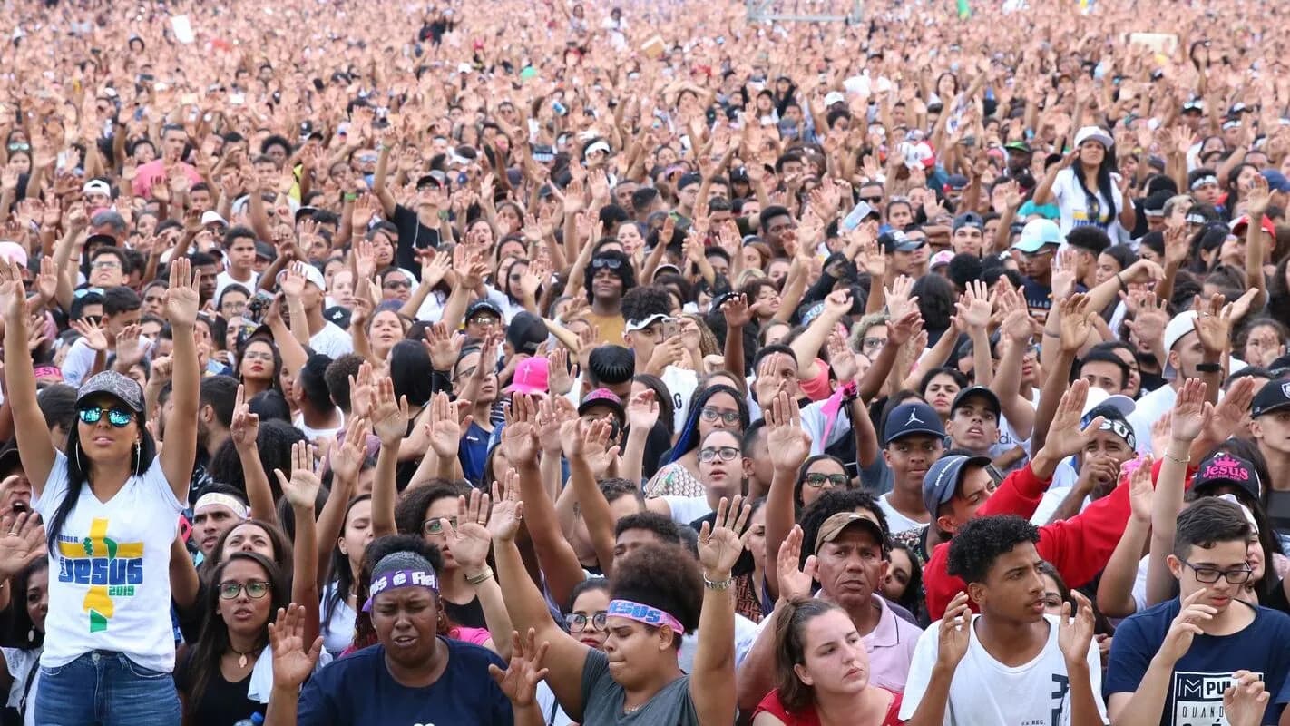 Multidão de fiéis evangélicos com as mãos erguidas durante culto ao ar livre