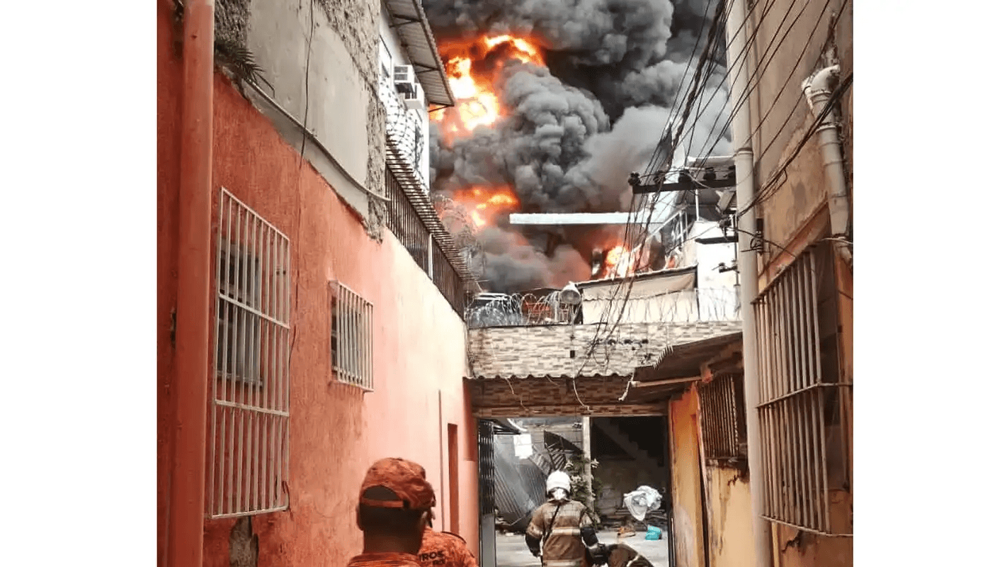 Bombeiros próximos a um grande incêndio industrial com densa fumaça preta (imagem de arquivo de ocorrência semelhante no Rio de Janeiro, em março de 2026 — não é do incêndio em Itaquaquecetuba)