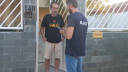 Recenseador do IBGE, identificado por camisa do instituto, entrevista morador em porta de casa