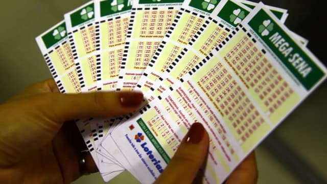 Mãos seguram vários bilhetes de aposta da Mega-Sena