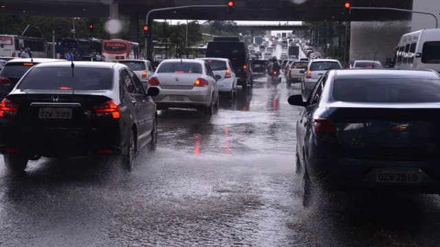 Trânsito de veículos na chuva em via urbana