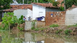 Pessoa próxima a águas de um rio junto a residências ribeirinhas