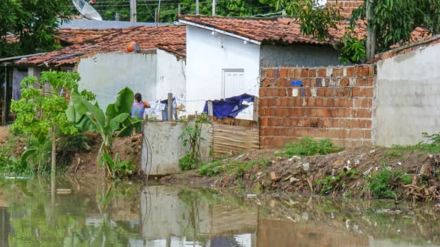 Pessoa próxima a águas de um rio junto a residências ribeirinhas