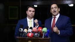 O senador Flávio Bolsonaro fala a jornalistas diante de microfones de emissoras de TV