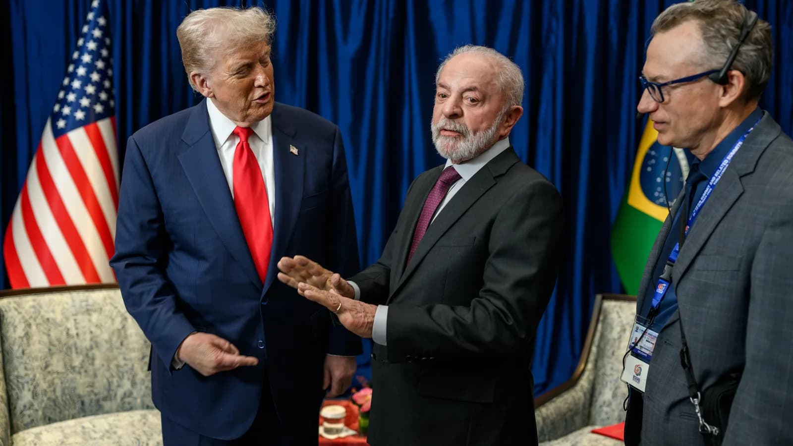 Donald Trump e Lula conversam lado a lado durante cúpula da Asean em Kuala Lumpur, com bandeiras dos EUA e do Brasil ao fundo