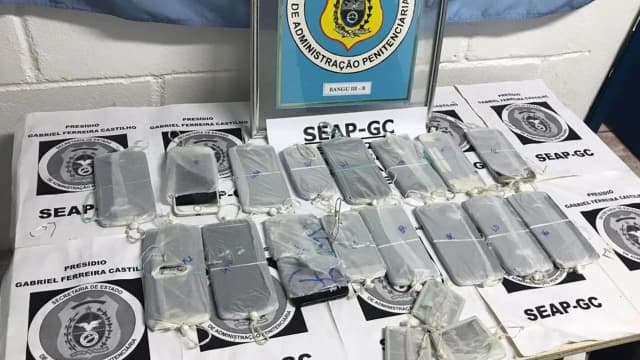 Celulares e outros materiais apreendidos em unidade prisional, organizados sobre mesa com etiquetas de identificação