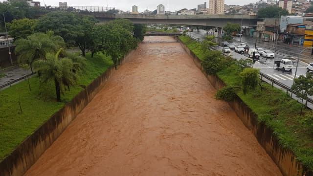 Córrego transbordando com água barrenta em via de Belo Horizonte durante temporal