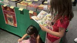 Duas crianças leem revistas em quadrinhos sentadas em evento literário