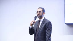 Homem de terno apresenta resultados de pesquisa em telão durante evento