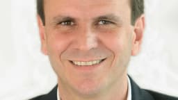 Retrato oficial de Eduardo Paes, candidato ao governo do Rio de Janeiro, sorrindo de terno escuro