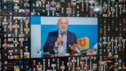 Lula durante transmissão ao vivo, com mosaico de espectadores ao fundo e placa com o número 13