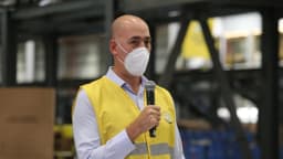 Funcionário do Mercado Livre em colete amarelo da empresa fala ao microfone dentro de um centro de distribuição