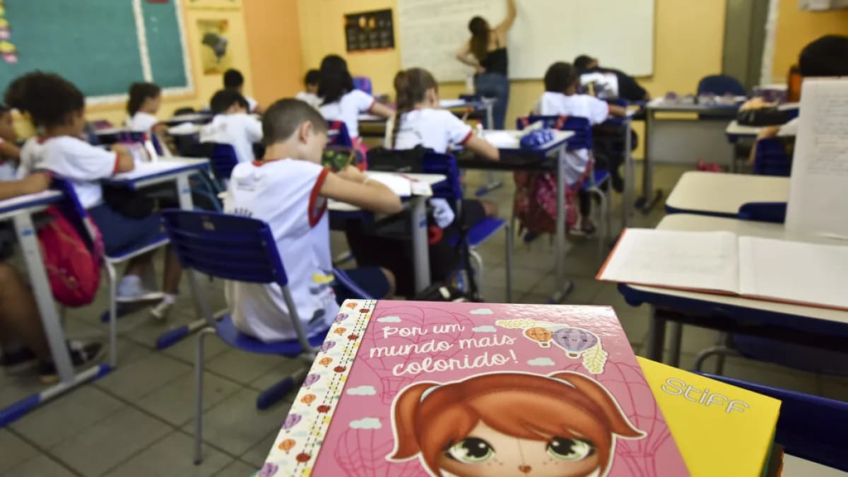 Sala de aula com alunos e professor escrevendo no quadro ao fundo