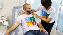 Homem doando sangue em hemocentro, deitado em maca, com profissional de saúde ao lado