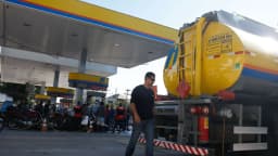 Caminhão-tanque abastecendo posto de combustível, com funcionário ao lado