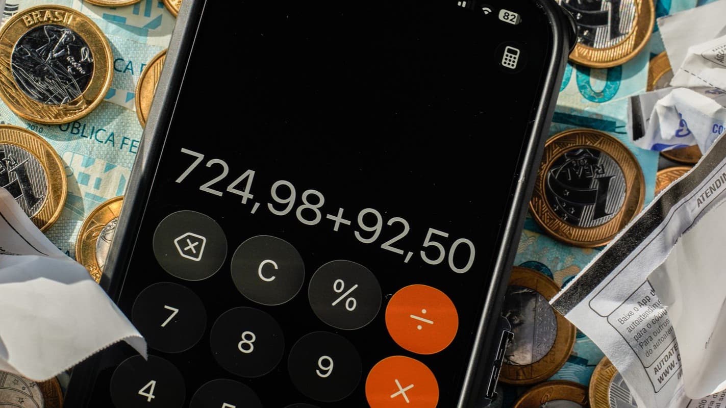 Calculadora do celular sobre dinheiro e comprovantes, simbolizando o aperto no orçamento das famílias