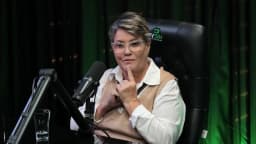 Cássia Barbosa, com a mão no queixo, fala pensativa durante entrevista no estúdio da TV Sim Brasil