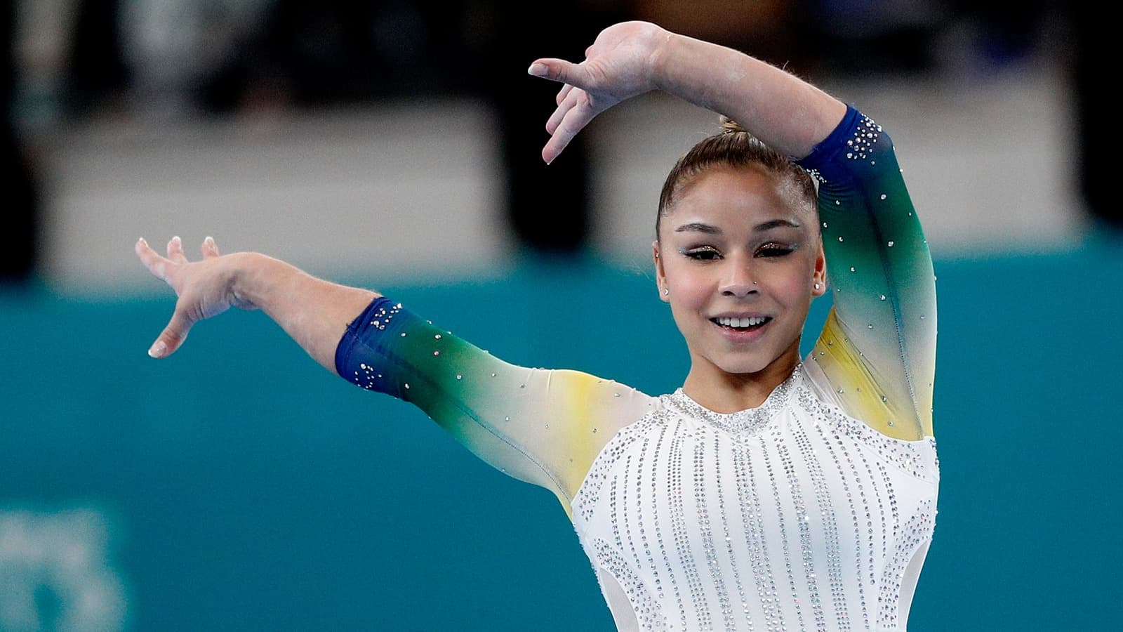 Flávia Saraiva sorri durante apresentação de ginástica artística, com uniforme branco e verde-amarelo