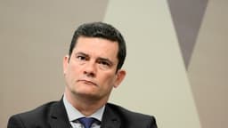 Retrato de Sérgio Moro em plano fechado, de terno escuro e gravata azul, com expressão séria e fundo neutro do Senado. Imagem de arquivo.