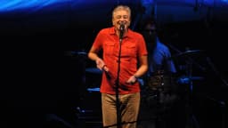 Caetano Veloso cantando sozinho no palco, com banda ao fundo