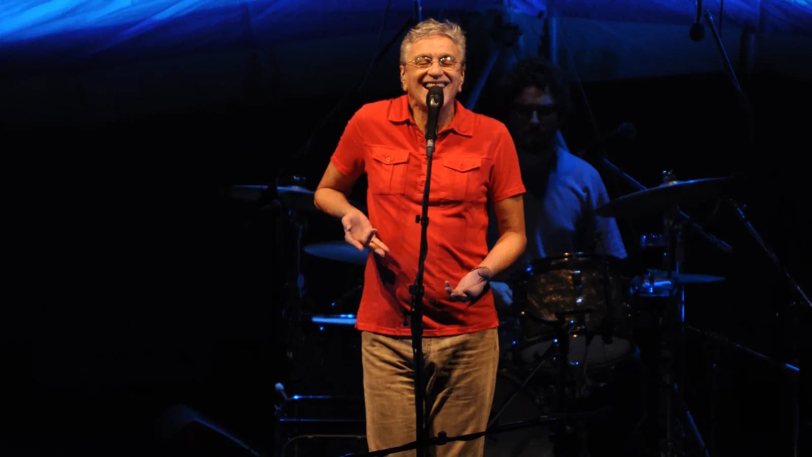 Caetano Veloso cantando sozinho no palco, com banda ao fundo