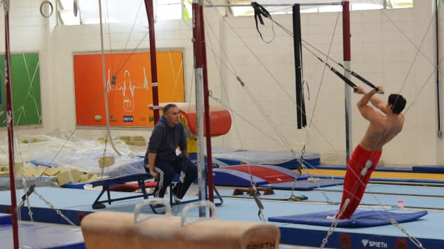 Ginasta brasileiro treina nas argolas em ginásio, observado por técnico (imagem de arquivo, 2016, preparação para os Jogos Olímpicos do Rio)