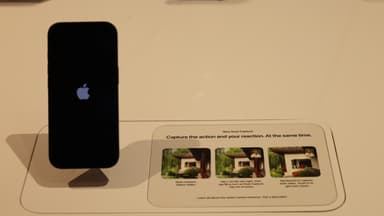 Aparelho iPhone exposto em suporte de vidro dentro de uma loja da Apple, ao lado de um cartaz explicativo sobre recursos de câmera. Foto de arquivo, sem relação direta com o programa Apple Upgrade.
