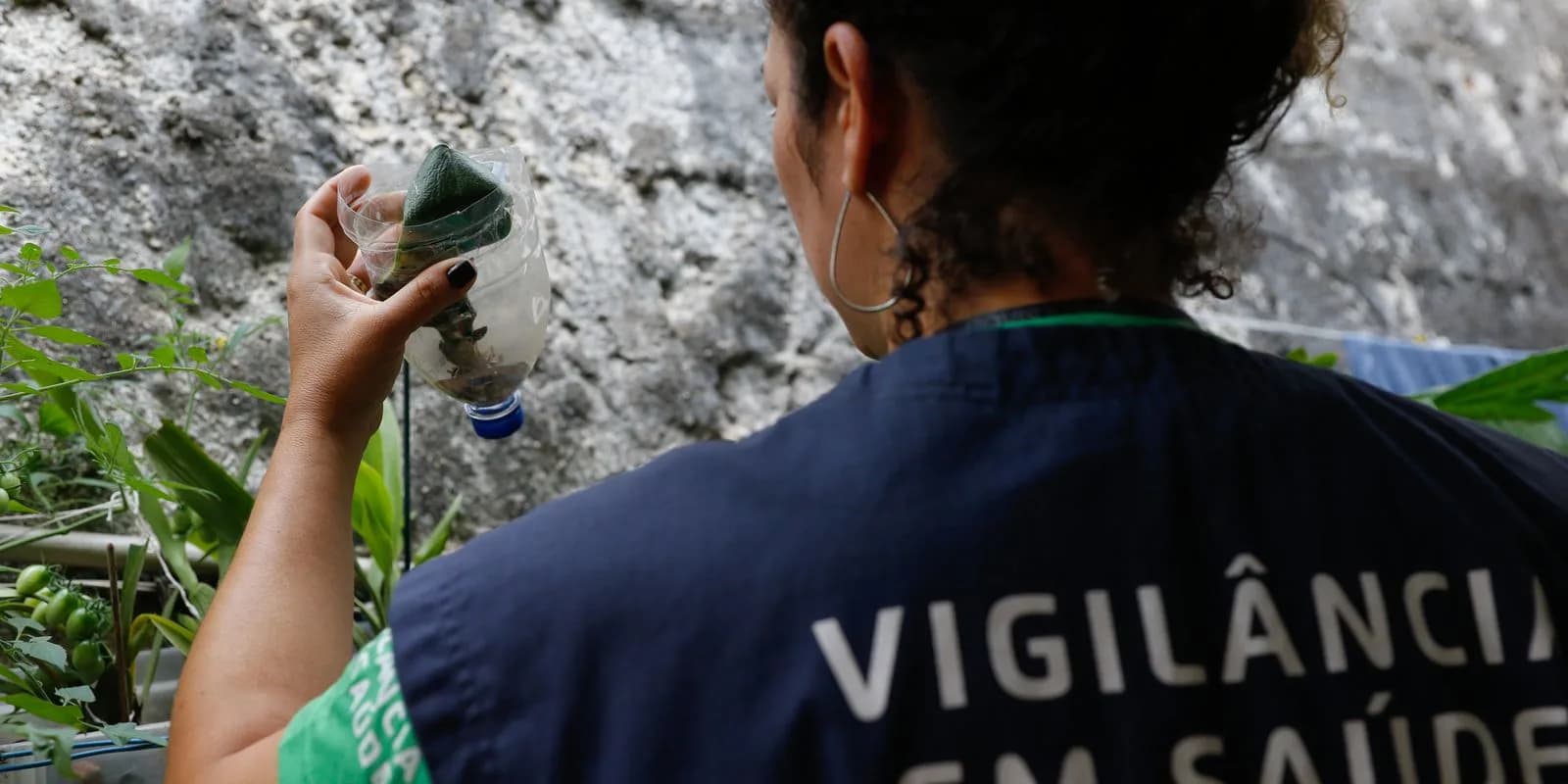 Agente de vigilância em saúde inspeciona garrafa com água parada em busca de foco do mosquito Aedes aegypti