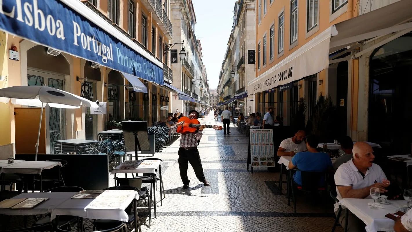 Rua movimentada no centro de Lisboa, em Portugal, com turistas e moradores em mesas de restaurante ao ar livre