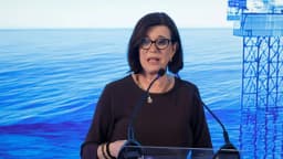 Executiva discursa em evento com imagem de plataforma de gás natural ao fundo