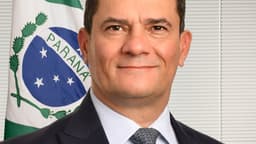 Retrato de Sergio Moro sorrindo, de terno, com a bandeira do Paraná ao fundo