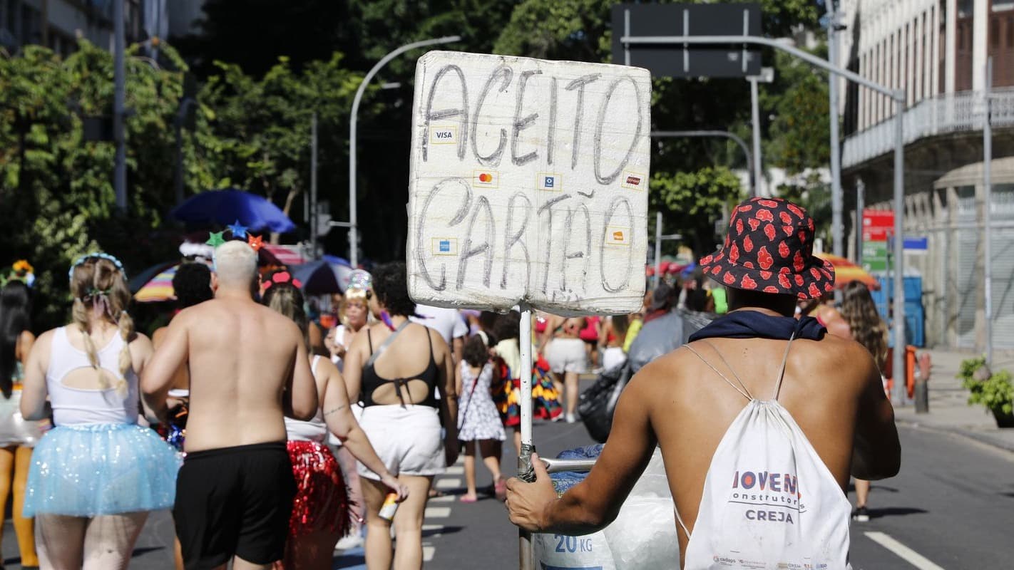 Vendedor ambulante carrega cartaz "Aceito cartão" durante bloco de carnaval no Rio de Janeiro, foto de arquivo