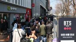 Fãs do BTS em fila com cartaz do grupo durante evento da turnê Arirang