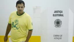 Eleitor com camisa verde-amarela caminha para a cabine de votação, sob placa da Justiça Eleitoral