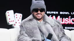 Bad Bunny sorri em coletiva de imprensa do Super Bowl LX Halftime Show, usando touca cinza e casaco de pelúcia