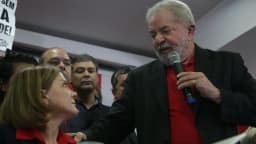 Lula fala ao microfone cercado de apoiadores em coletiva de imprensa