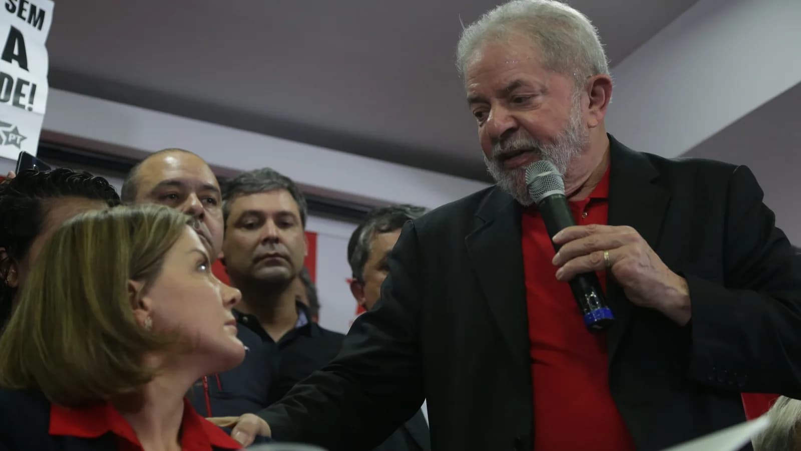 Lula fala ao microfone cercado de apoiadores em coletiva de imprensa