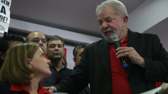 Lula fala ao microfone cercado de apoiadores em coletiva de imprensa