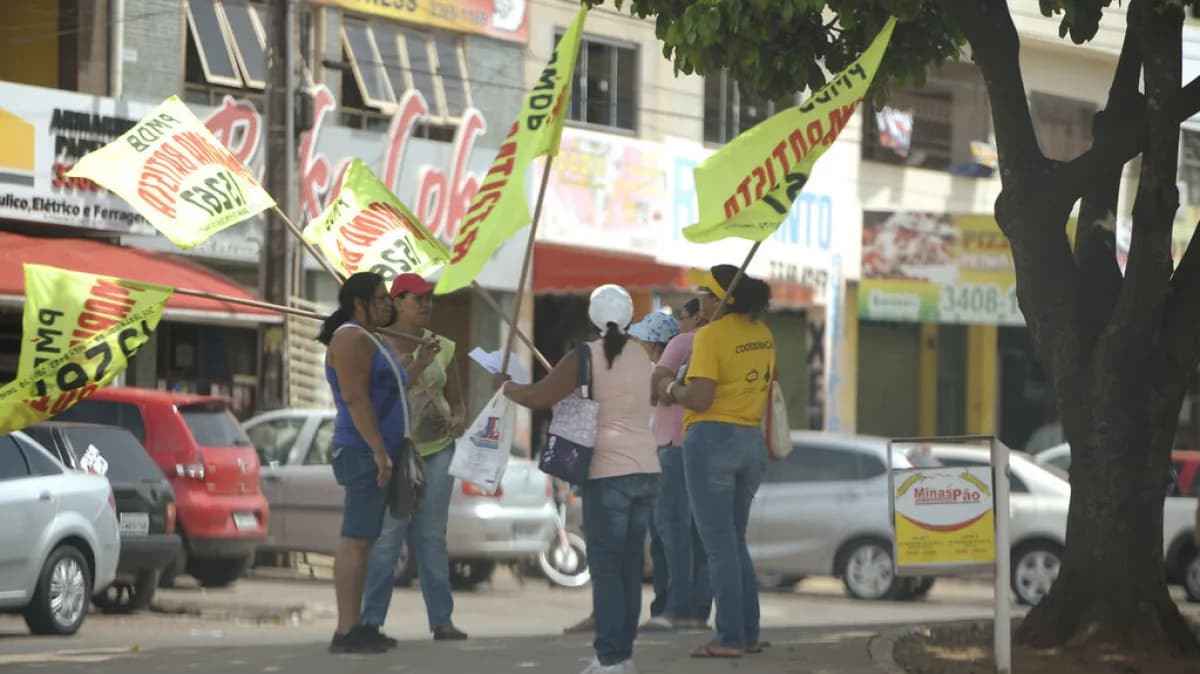 Pessoas seguram bandeiras e materiais de propaganda eleitoral em rua movimentada
