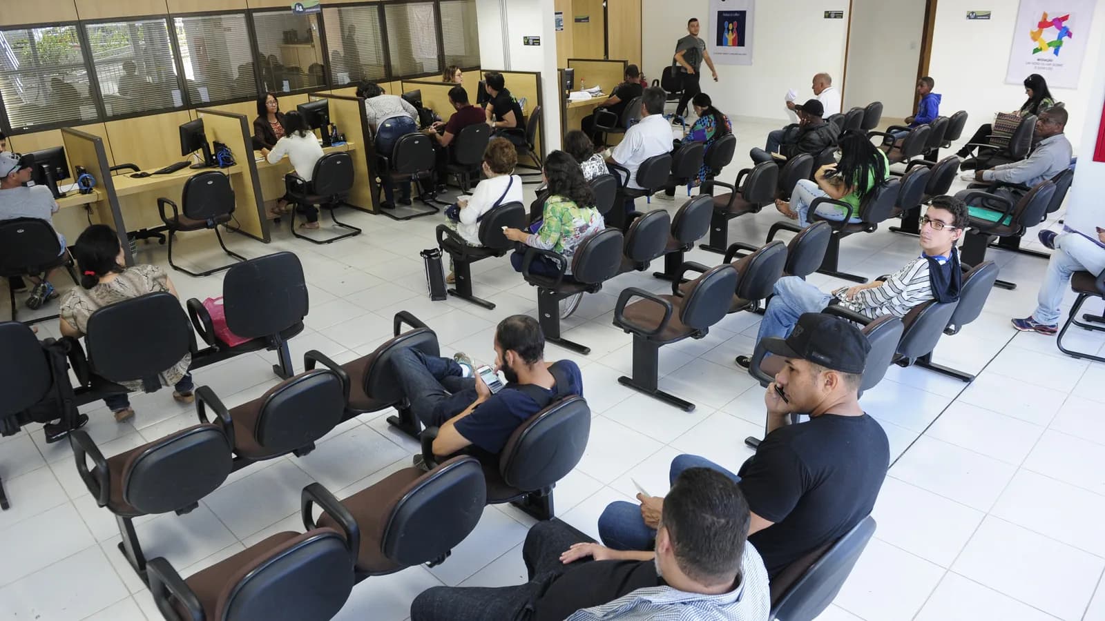 Sala de atendimento ao público na sede da Defensoria Pública do Distrito Federal, com pessoas aguardando em cadeiras