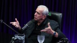 Ricardo Teagano ergue as duas mãos abertas perto do rosto, em gesto de surpresa, durante a entrevista em estúdio