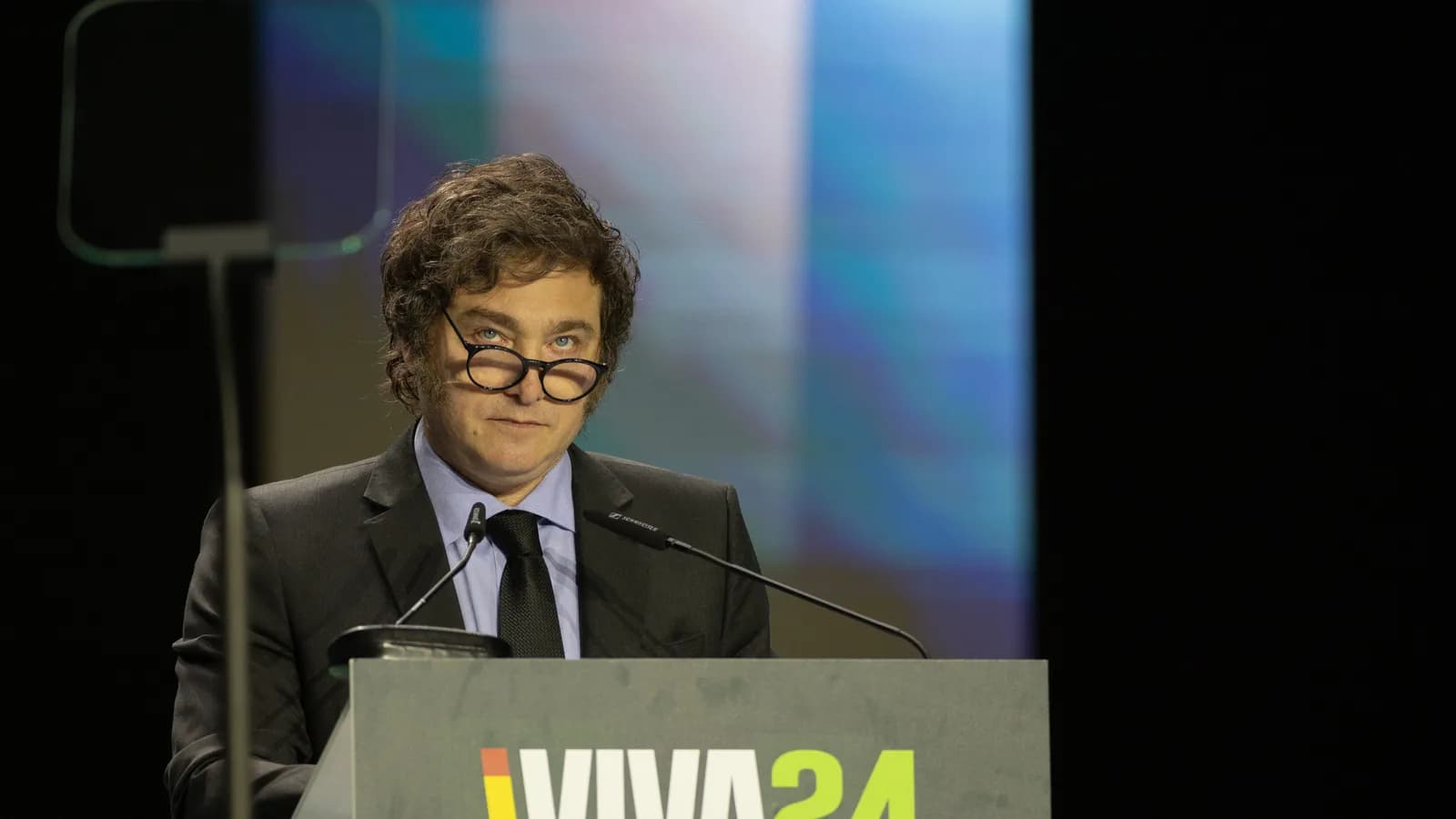 Javier Milei discursa em evento, com as mãos apoiadas em um púlpito