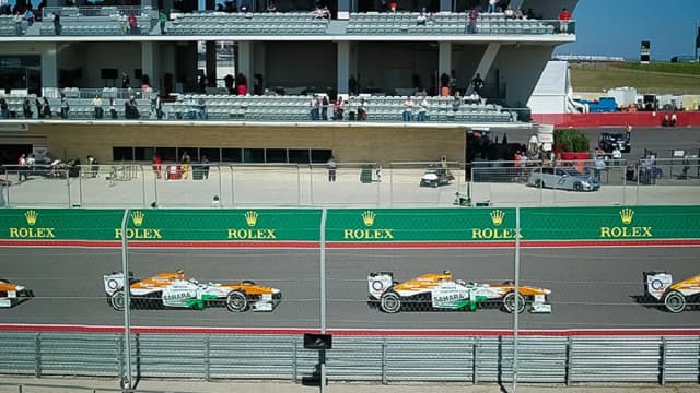 Carros de Fórmula 1 em disputa de ultrapassagem na pista do Circuito das Américas, em Austin, com arquibancada ao fundo
