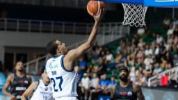 Jogador de basquete arremessa a bola próximo à cesta durante partida profissional
