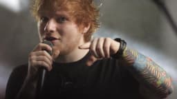 Ed Sheeran cantando ao microfone durante apresentação ao vivo