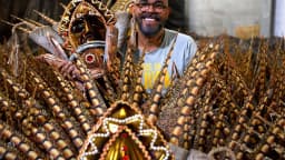 Carnavalesco sorri ao lado de fantasia com penas douradas em preparação para desfile