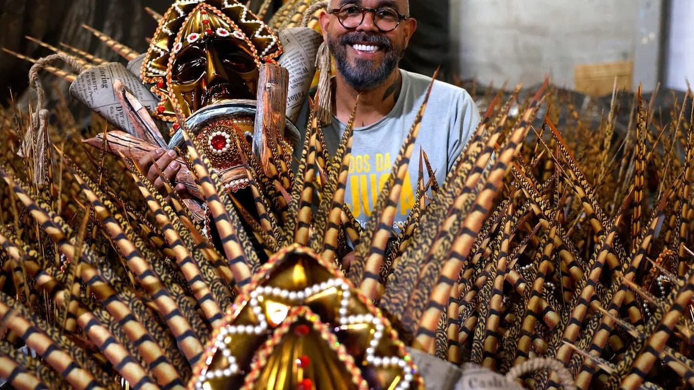 Carnavalesco sorri ao lado de fantasia com penas douradas em preparação para desfile